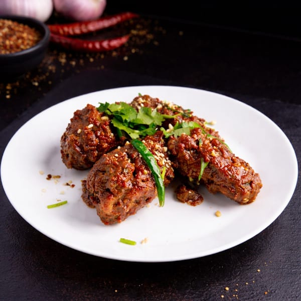 Spicy chicken wings garnished with cilantro and sesame seeds on a white plate.